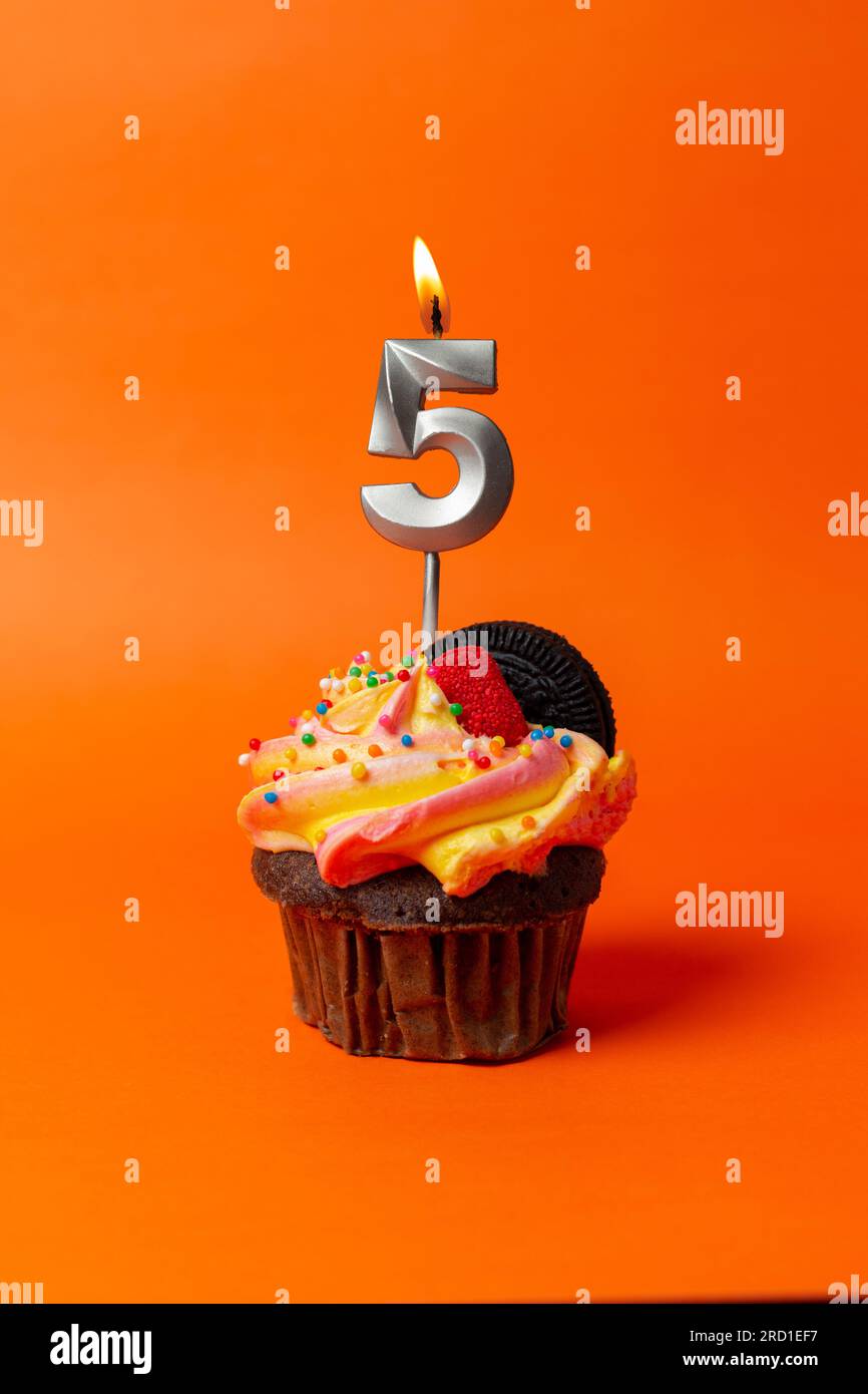Geburtstagskuchen mit Nummer 5 - Cupcake auf orangefarbenem Hintergrund mit Geburtstagskerzen Stockfoto