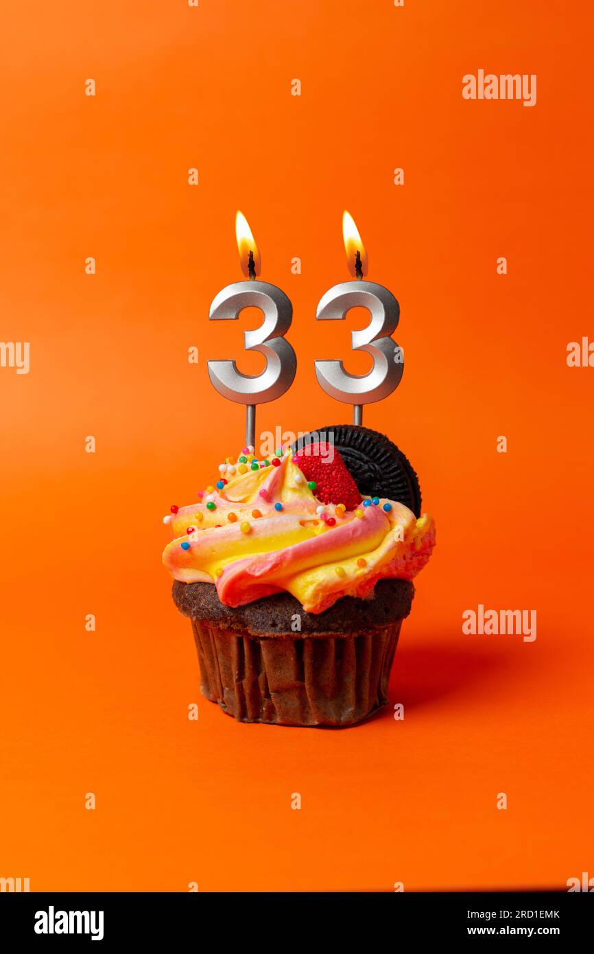 Geburtstagskuchen mit Nummer 33 - Cupcake auf orangefarbenem Hintergrund mit Geburtstagskerzen Stockfoto