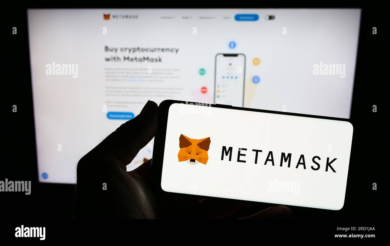 Person, die ein Smartphone mit dem Logo der Kryptowährung-Geldbörse-Software MetaMask auf dem Bildschirm vor der Website hält. Konzentrieren Sie sich auf das Display des Telefons. Stockfoto