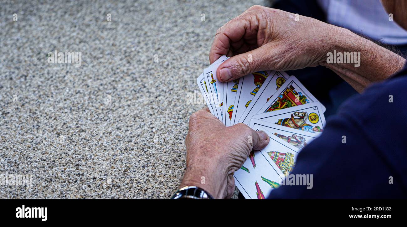 Ältere und pensionierte Person, die mit einem Kartendeck spanischer Karten auf einem Granitsteintisch in einem ländlichen Bergdorf spielt Stockfoto