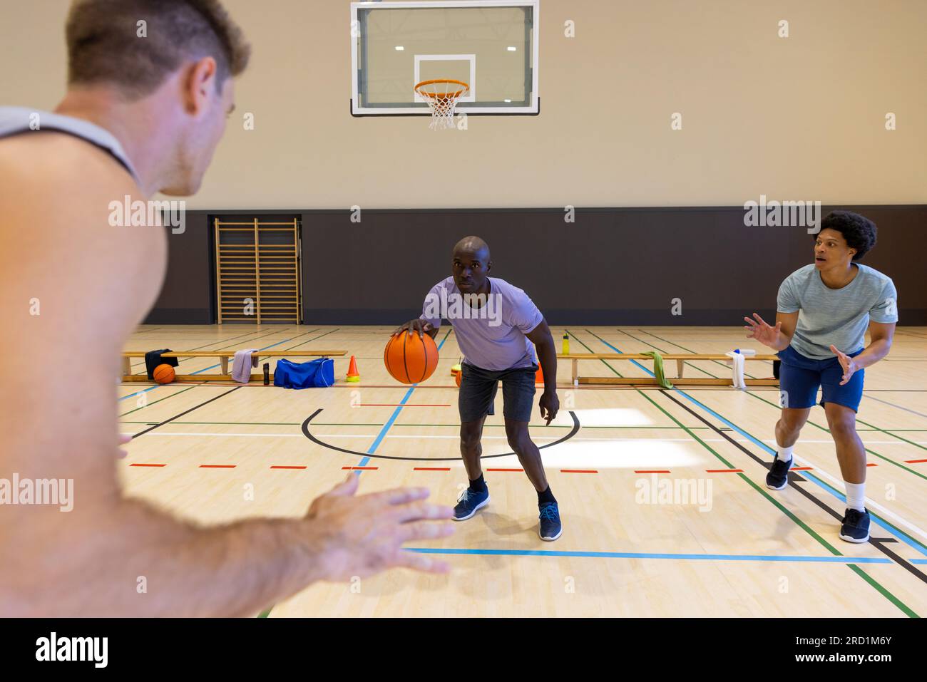 Verschiedene männliche Basketballspieler, die graue Sportkleidung tragen und im Fitnessstudio Basketball spielen Stockfoto