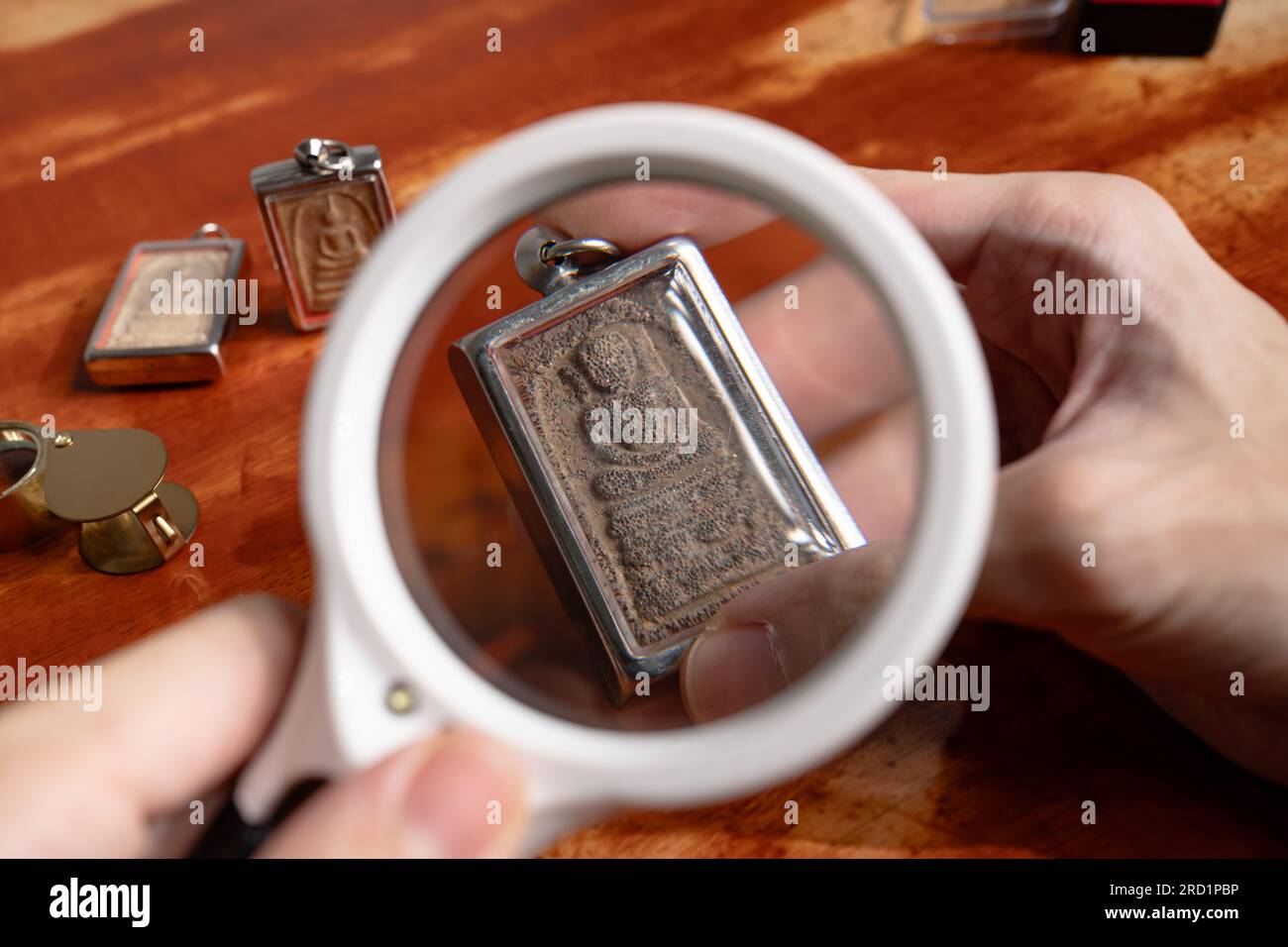 Mit einer Lupe sehen Sie die Details auf einem alten thailändischen Buddha-Amulett Stockfoto