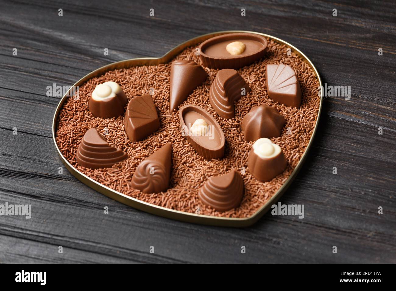 Schokoladenbonbons in Schokoladenstückchen in einer herzförmigen Schachtel auf dunklem Holzhintergrund, Nahaufnahme zum Valentinstag. Stockfoto