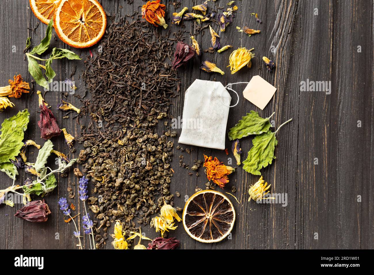 Zusammensetzung von trockenem schwarzen und grünen Tee, Teebeutel, getrockneten Zitrusscheiben und trockenen Hibiskusblumen auf dunklem Holzhintergrund von oben. Stockfoto