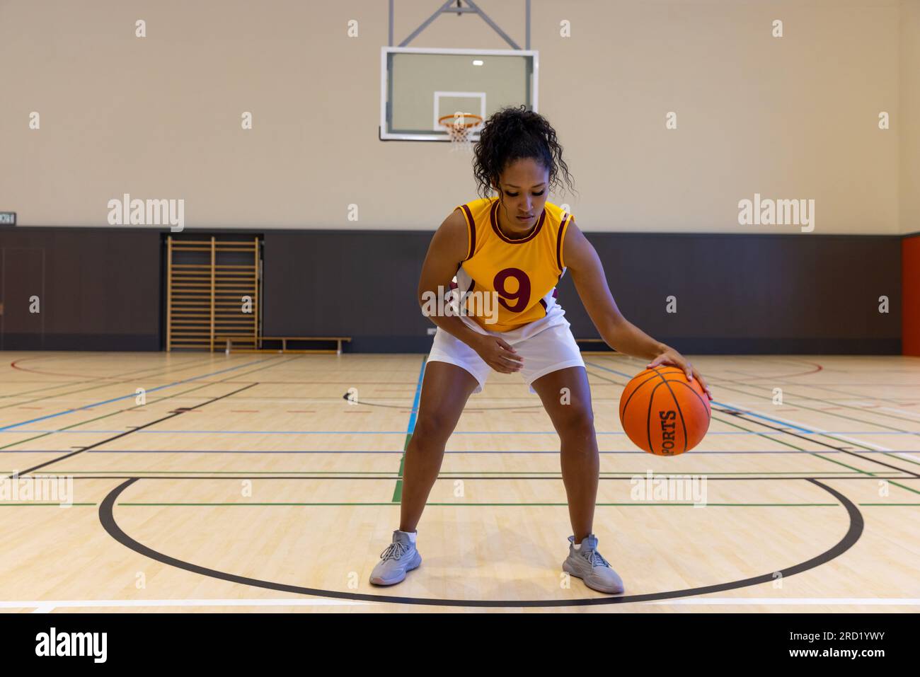 Fokussierte Basketballspielerin, die Sportkleidung mit Nummer trägt und im Fitnessstudio Basketball spielt Stockfoto