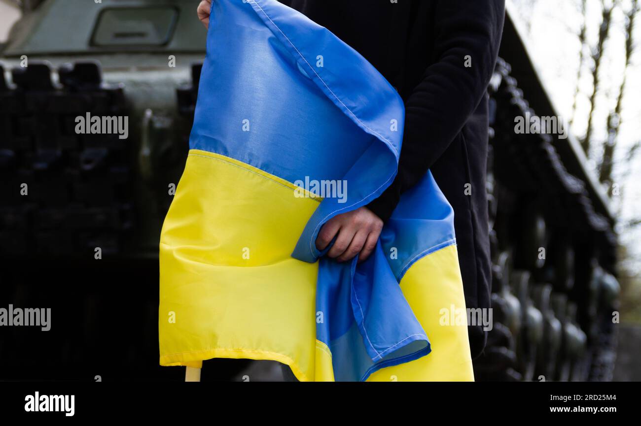 Frau mit ukrainischer Flagge, Kampfpanzer im Hintergrund. Protest gegen die russische Invasion, Krieg in der Ukraine. Krisenkonzept, Anti-Kriegs-Demonstration. Stockfoto