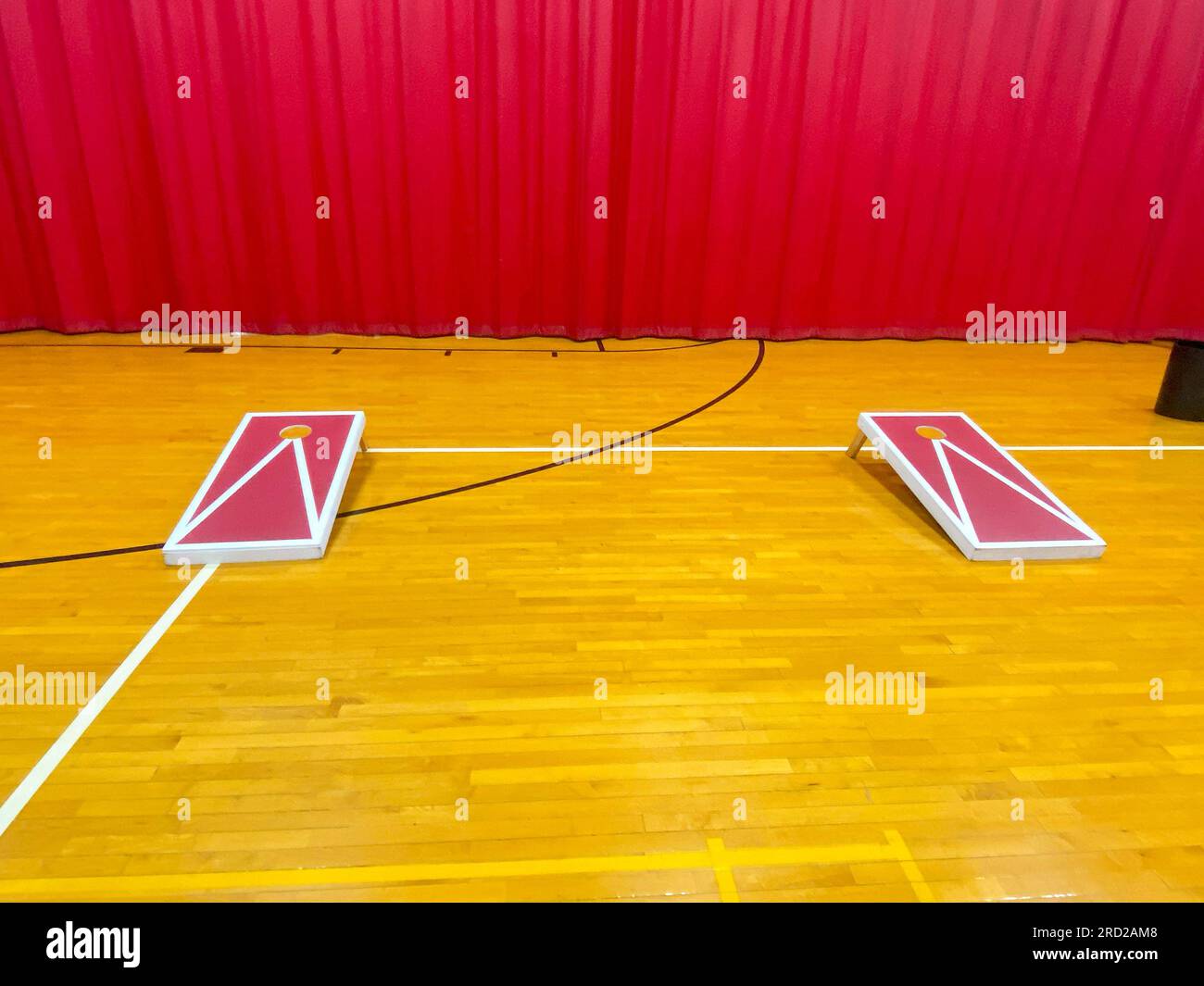 Vorderansicht von zwei hausgemachten Maislochbrettern auf einer Gymnastiketage mit einem roten Vorhang im Hintergrund. Stockfoto