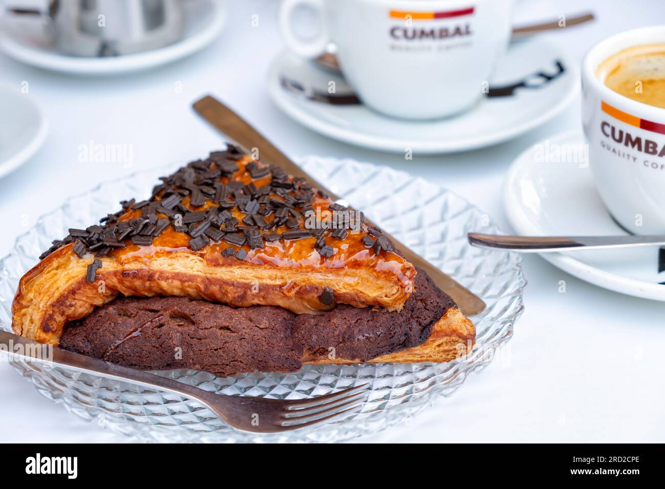Eine einzelne Portion einer großen, tiefen, dreieckigen Pain Au Chocolate oder Napolitanas, serviert mit Kaffee an einem Tisch vor einer Patisserie. Stockfoto