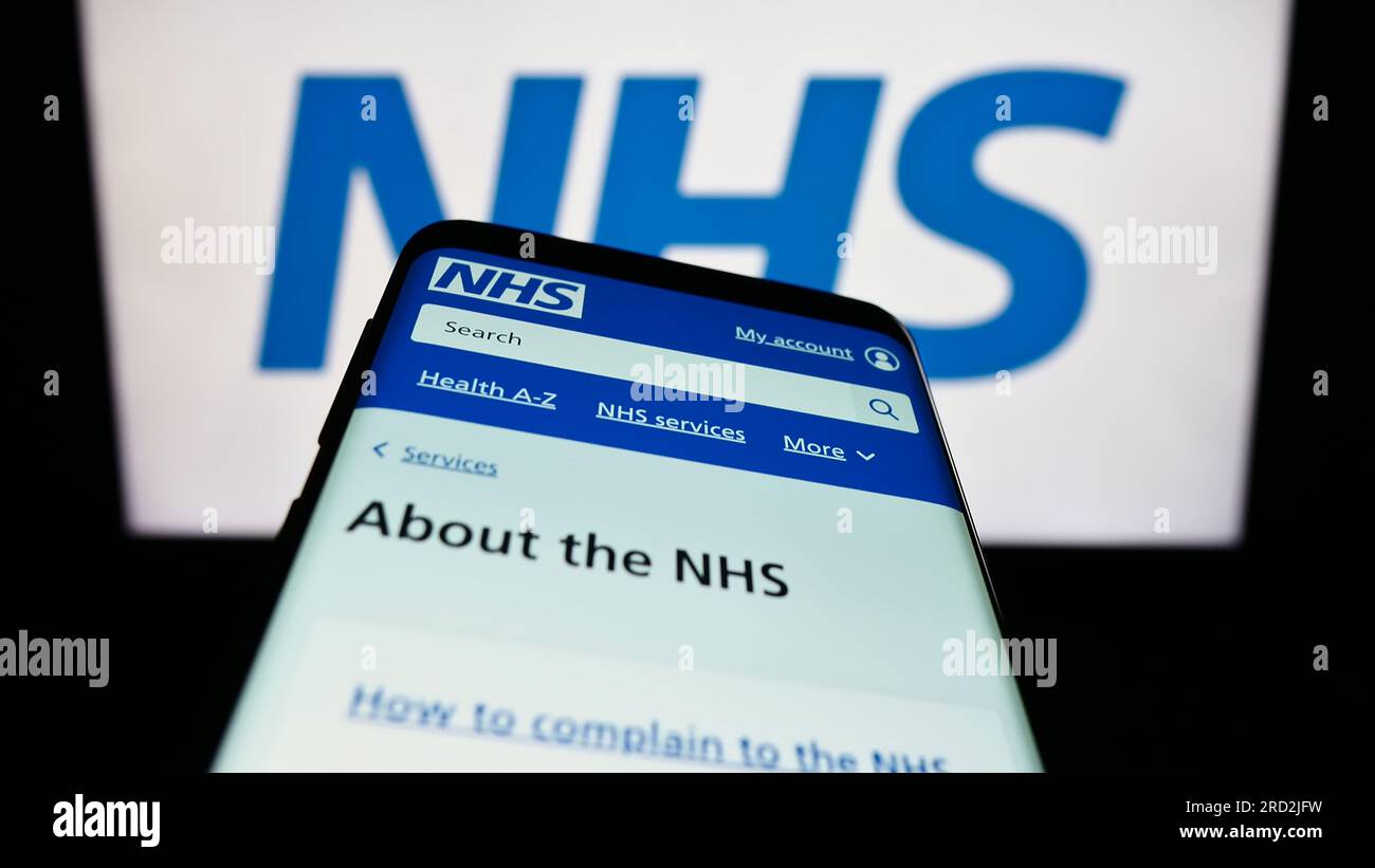 Mobiltelefon mit Website des British National Health Service (NHS) auf dem Bildschirm vor dem Logo. Fokus auf oberer linker Seite des Telefondisplays. Stockfoto
