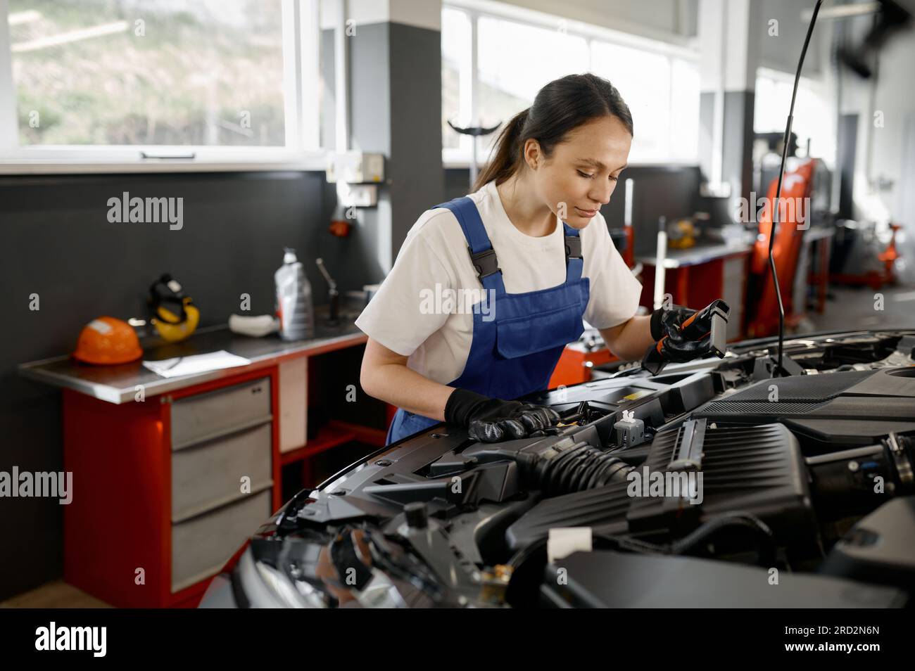 Junge Handwerkerin, die in einer Autowerkstatt am Motor arbeitet Stockfoto