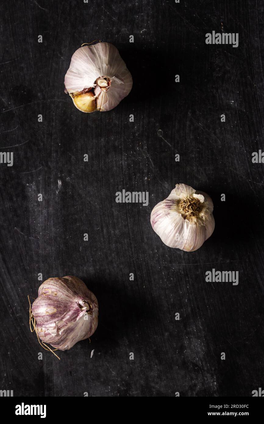 Frische Knoblauchknollen auf schwarzem Hintergrund. Flach verlegt. Draufsicht. Speisekonzept. Dunkle Stimmungsfotografie. Stockfoto