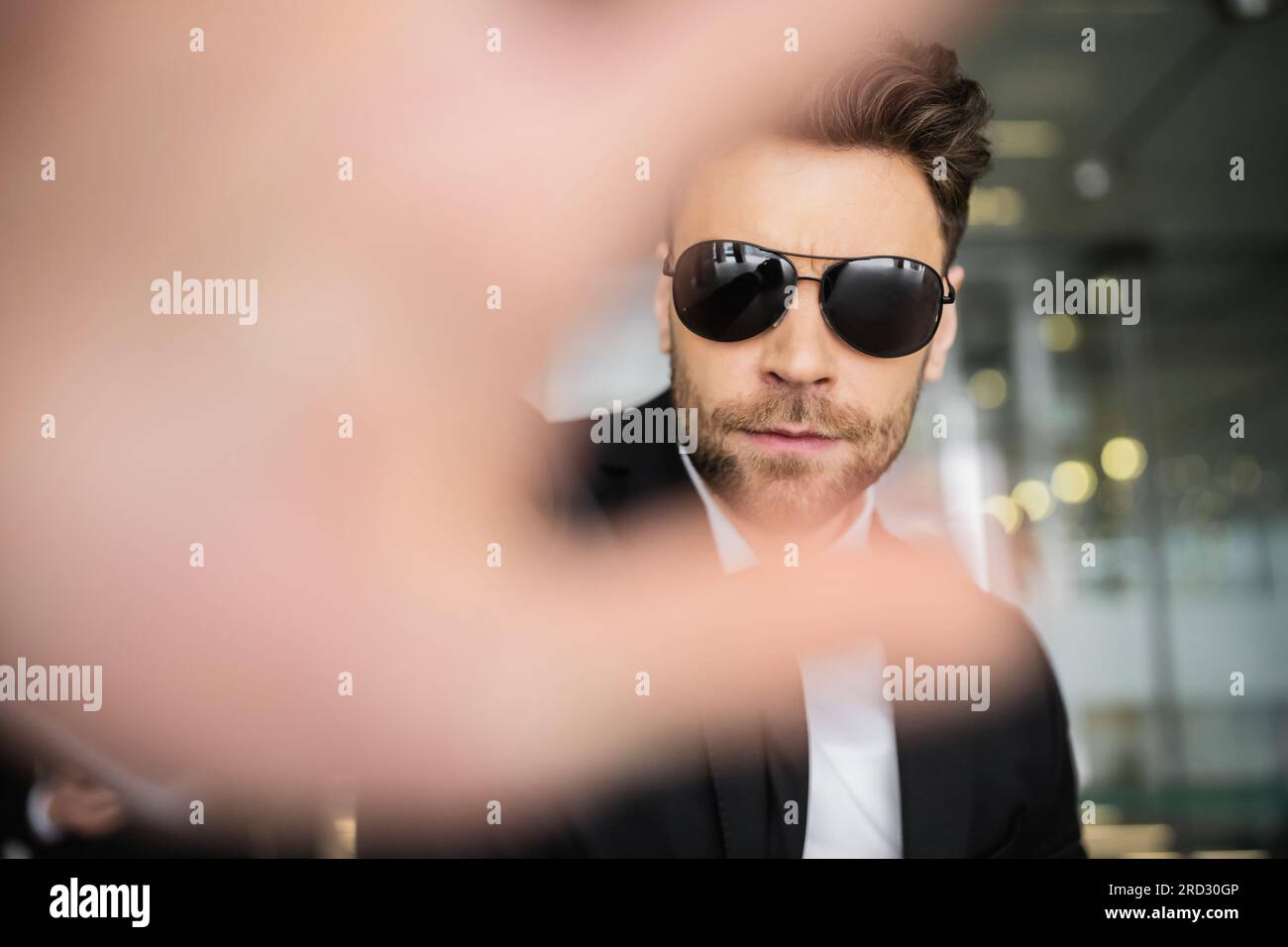 Stop-Geste, Bodyguard in dunkler Sonnenbrille und schwarzer Anzug, der in die Kamera schaut, Halt zeigt, Hotelsicherheit, Sicherheitsmanagement, uniformierter Wachmann im Dienst, Stockfoto