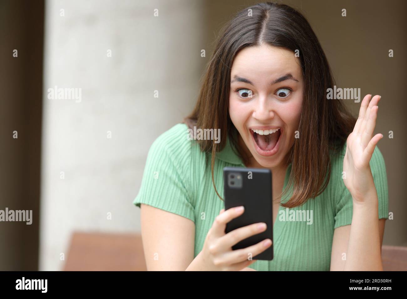 Aufgeregte Frau, die auf der Straße fantastische Inhalte am Telefon überprüft Stockfoto