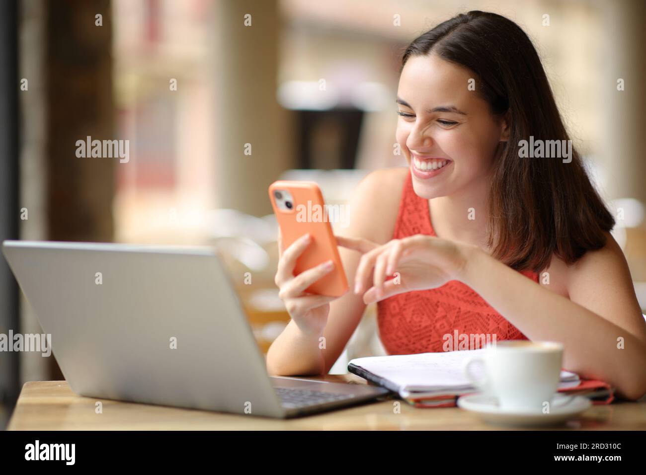 Glückliche Schülerin, die Smartphone und Computer auf der Barterrasse überprüfte Stockfoto