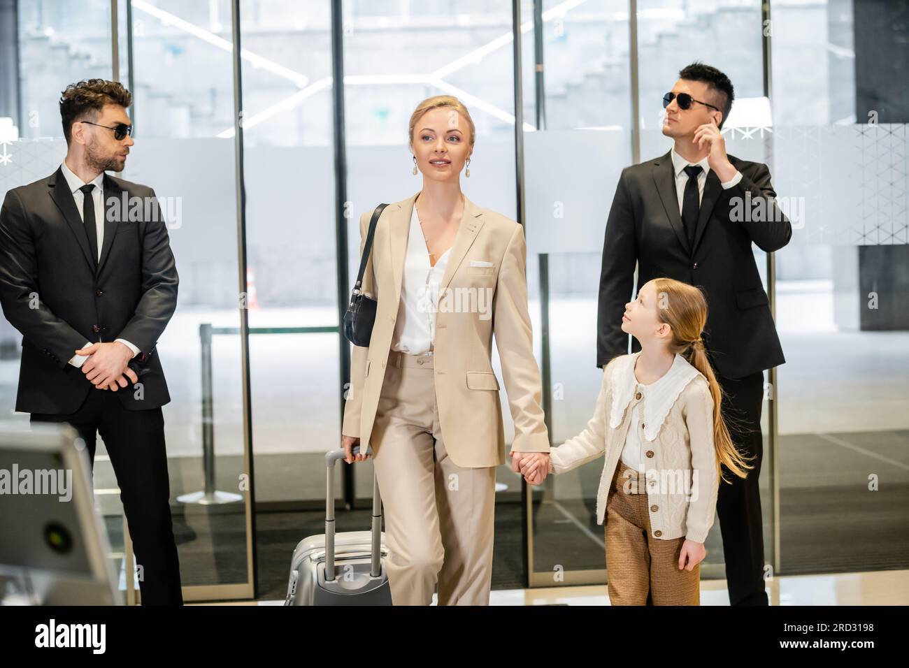 Luxuriöser Lifestyle, persönliches Sicherheitskonzept, zwei Bodyguards in Anzügen und Sonnenbrillen, die attraktive blonde Frau mit Kind-, Frauen- und Mädchenhalterung schützen Stockfoto