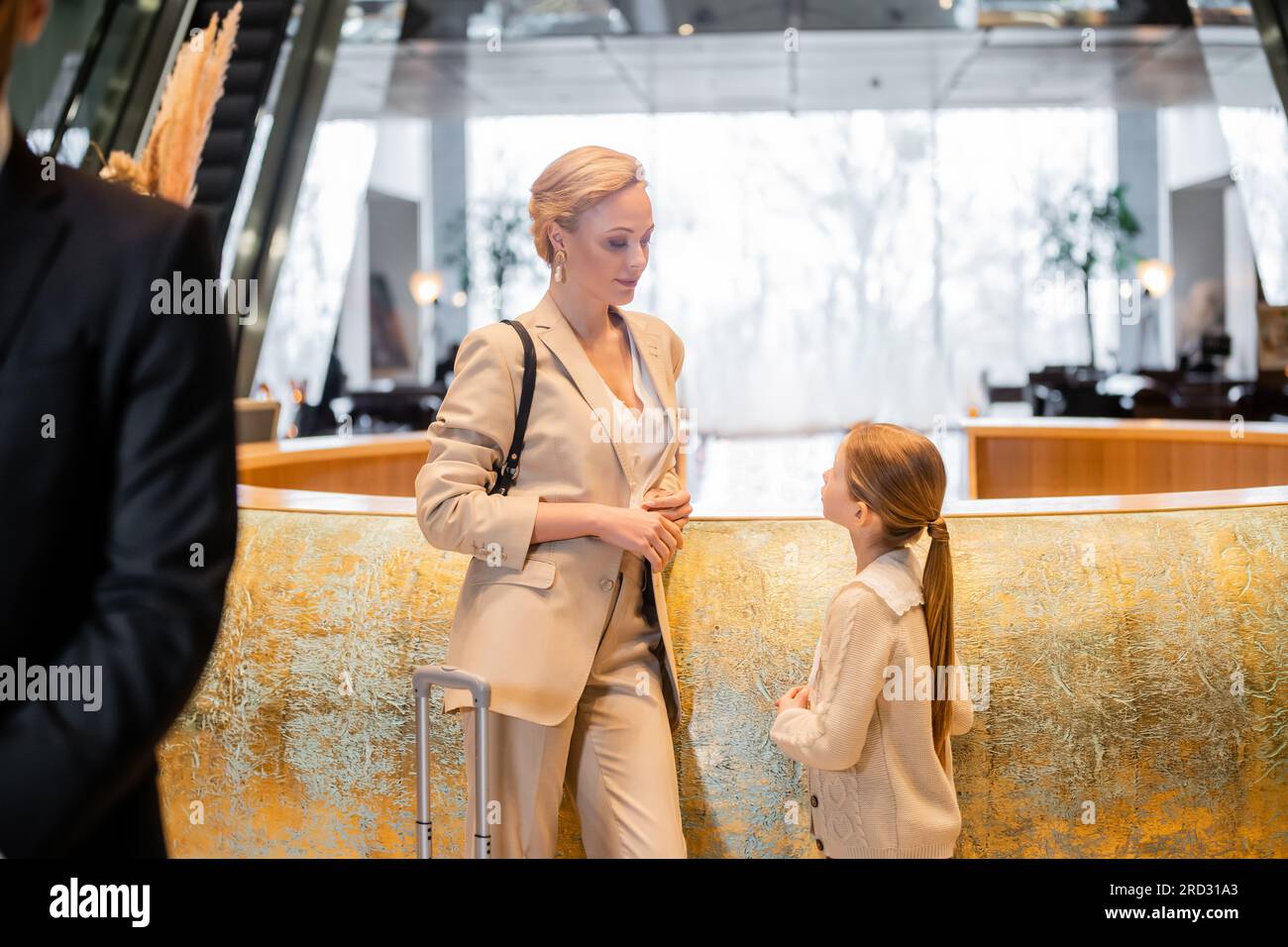 Familienreisen, blonde Frau, die an der Rezeption mit einer jungen Tochter steht, während des Check-ins über etwas spricht, Hotelbranche, Bodyguard steht Stockfoto