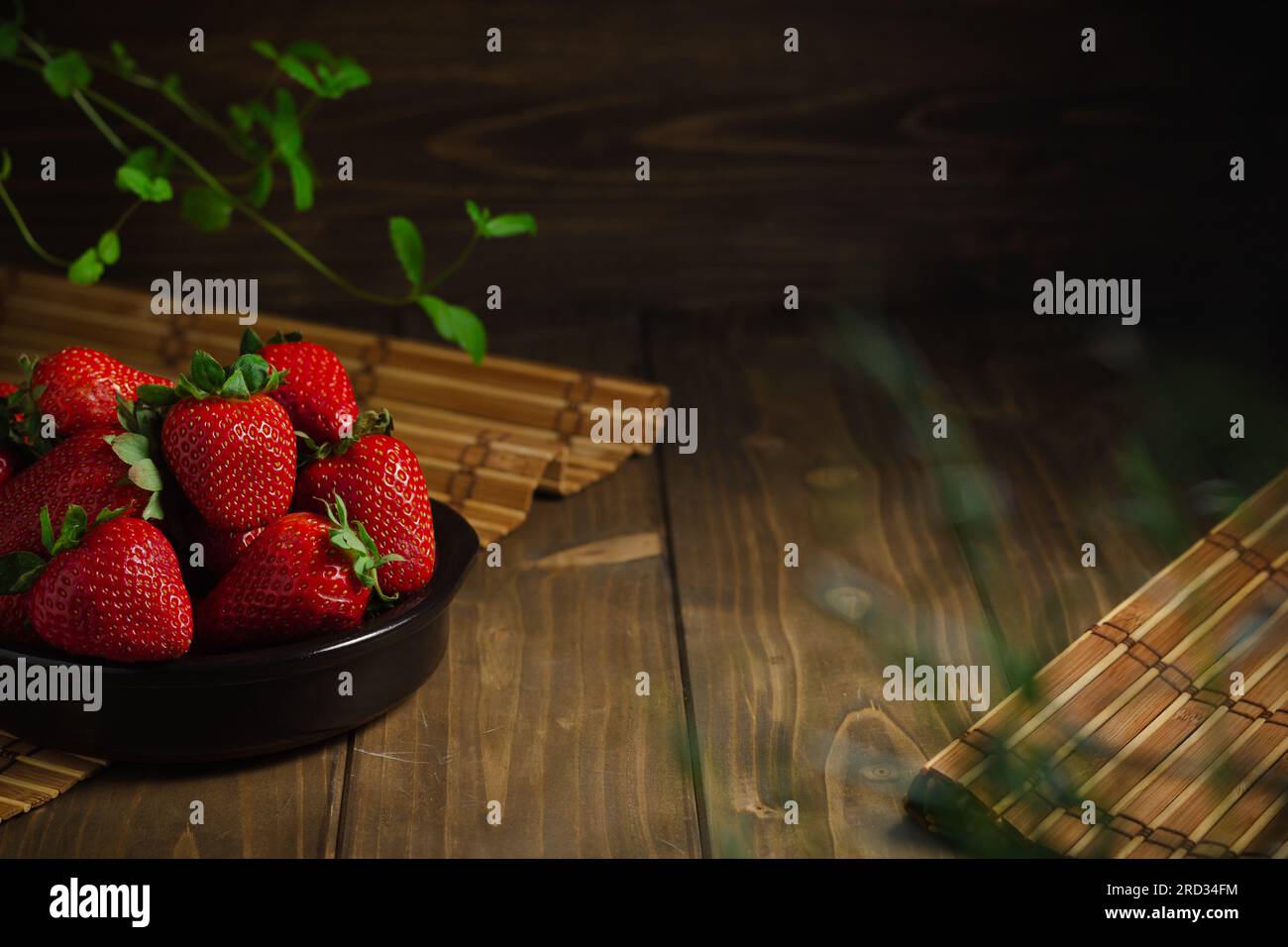 Köstliche frische Erdbeeren mit grünen Blättern in einer schwarzen Schüssel auf einem Holztisch mit Kopierbereich. Stockfoto