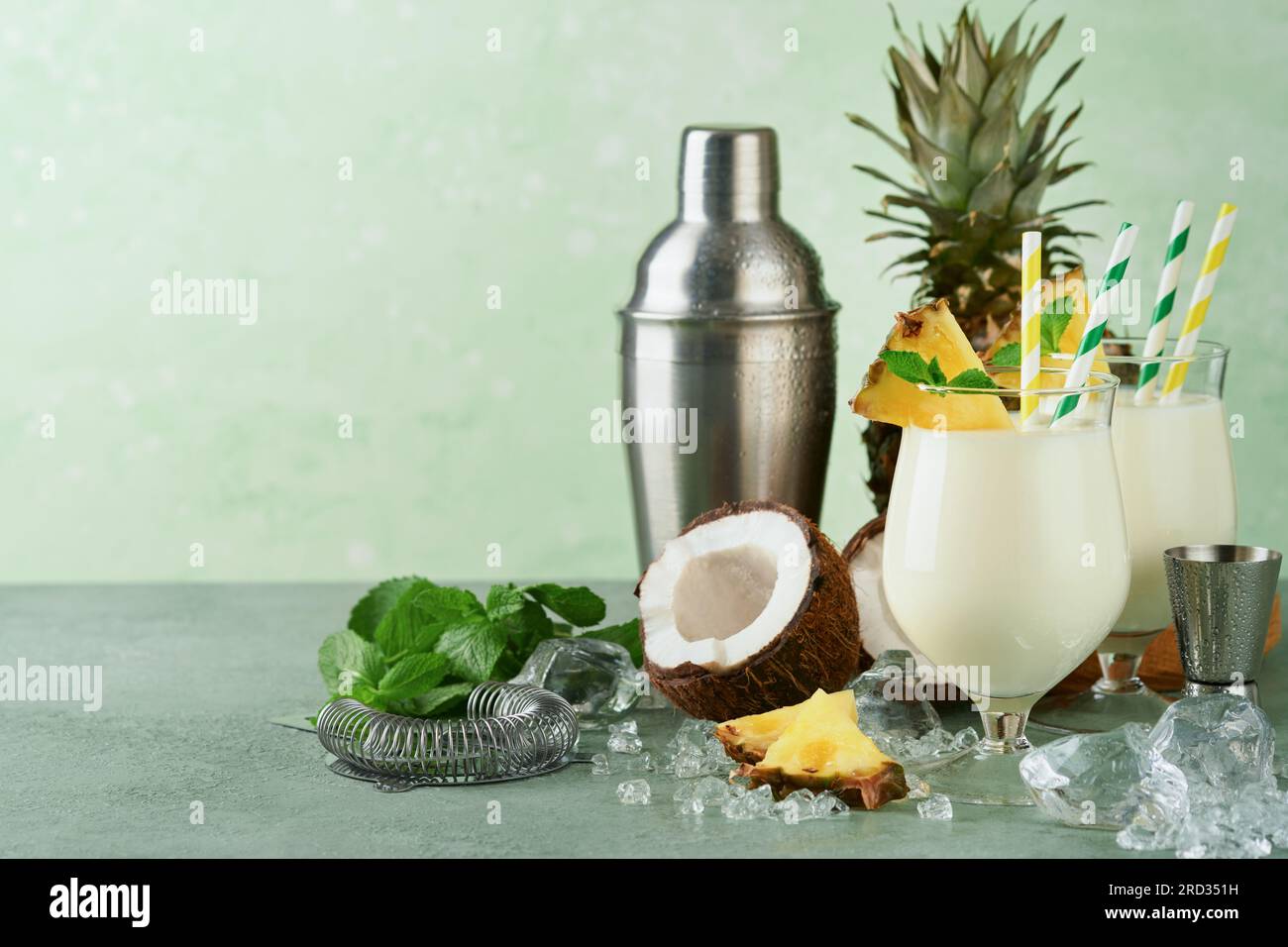 Pina Colada. Traditioneller karibischer Cocktail aus Rum, Ananassaft und Kokosnusscreme mit tropischen Früchten und Barutensilien auf frischem grünen Hintergrund. Stockfoto