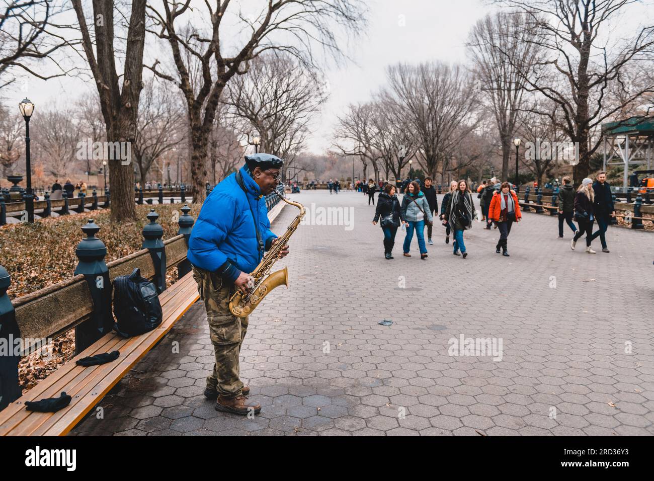 Straßenmusiker spielt Saxophon, während andere Passanten um ihn herumlaufen, Central Park, New York Stockfoto