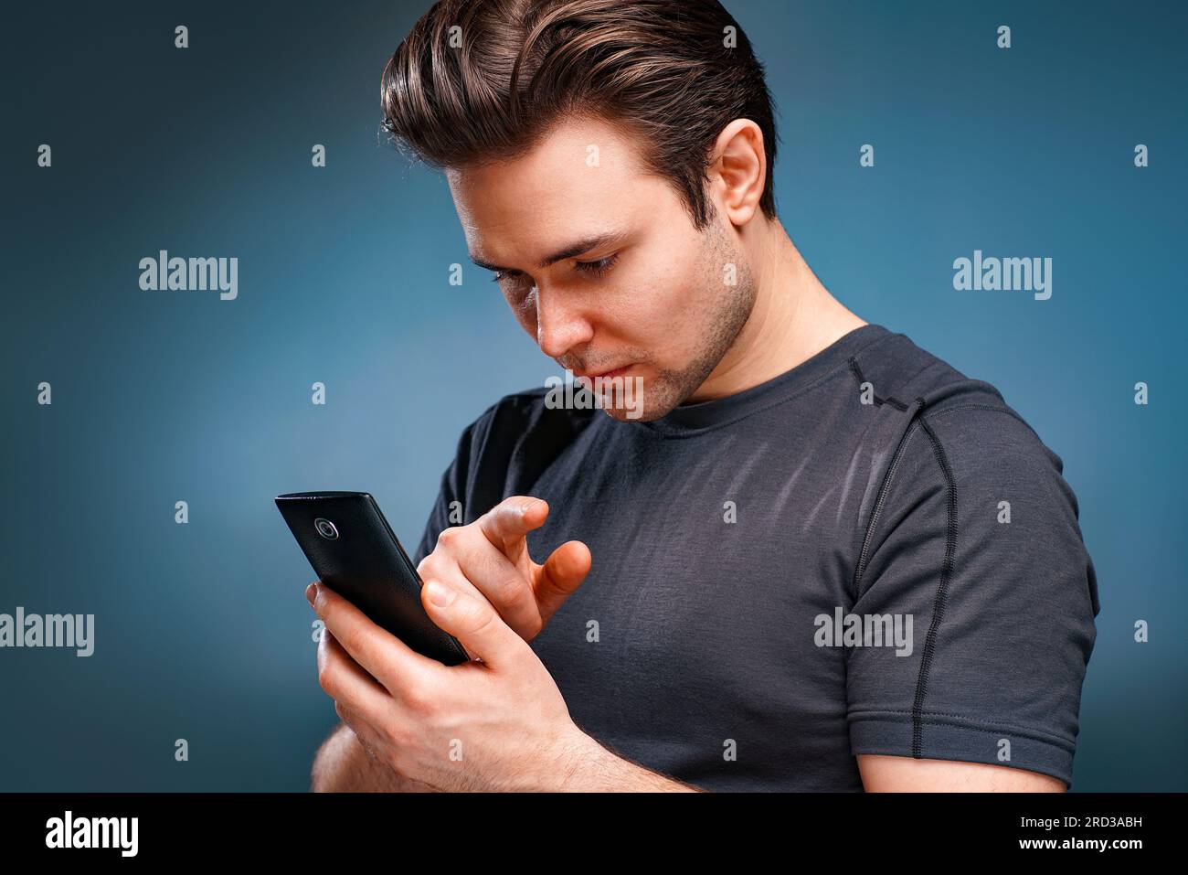 Ein junger Mann, der sich ein Telefonporträt auf grauem Hintergrund ansieht Stockfoto
