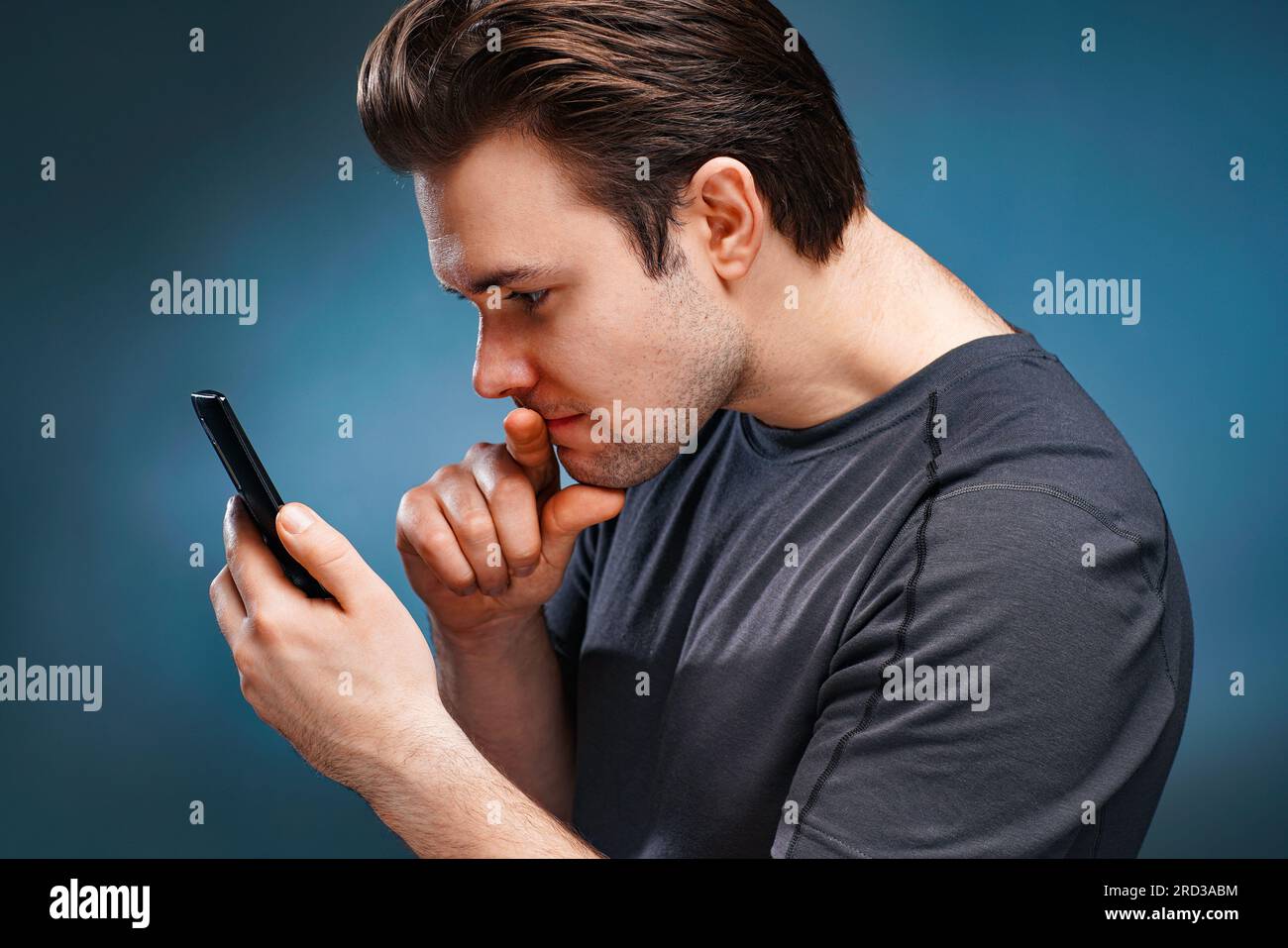 Ein junger Mann, der sich ein Telefonporträt auf grauem Hintergrund ansieht Stockfoto