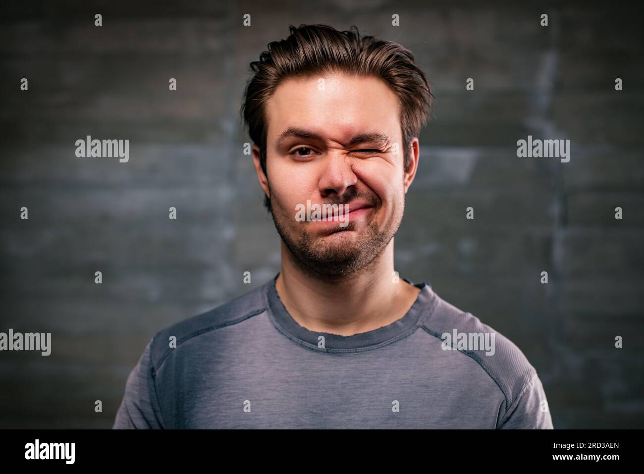 Ein junger gutaussehender Mann, der ein Porträt auf grauem Hintergrund blinzelt Stockfoto