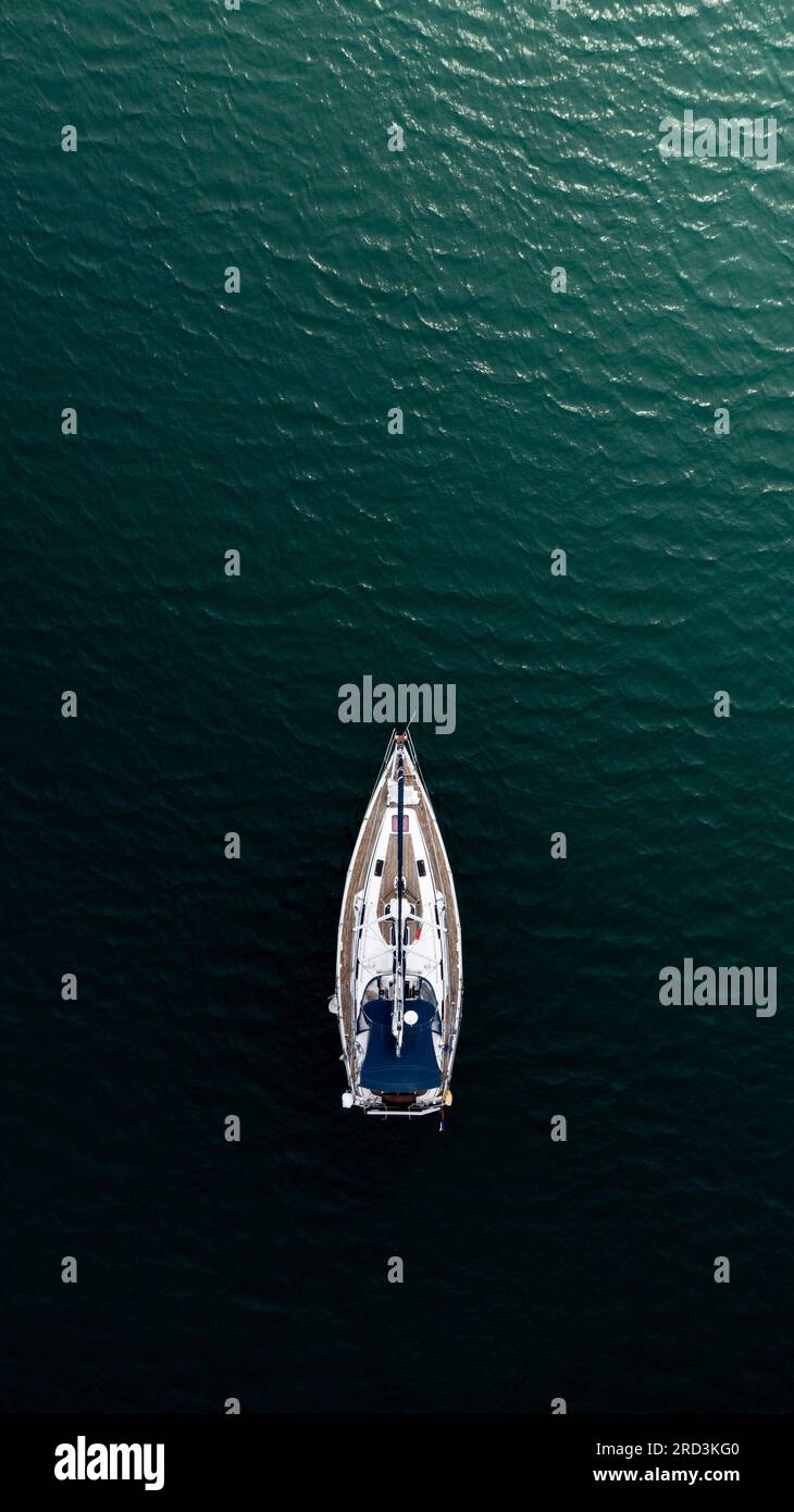 Aus der Vogelperspektive direkt über einer luxuriösen Segelyacht, die aus der Dunkelheit auftaucht und in Richtung des Lichts segelt, in einem Konzept der Hoffnung Stockfoto