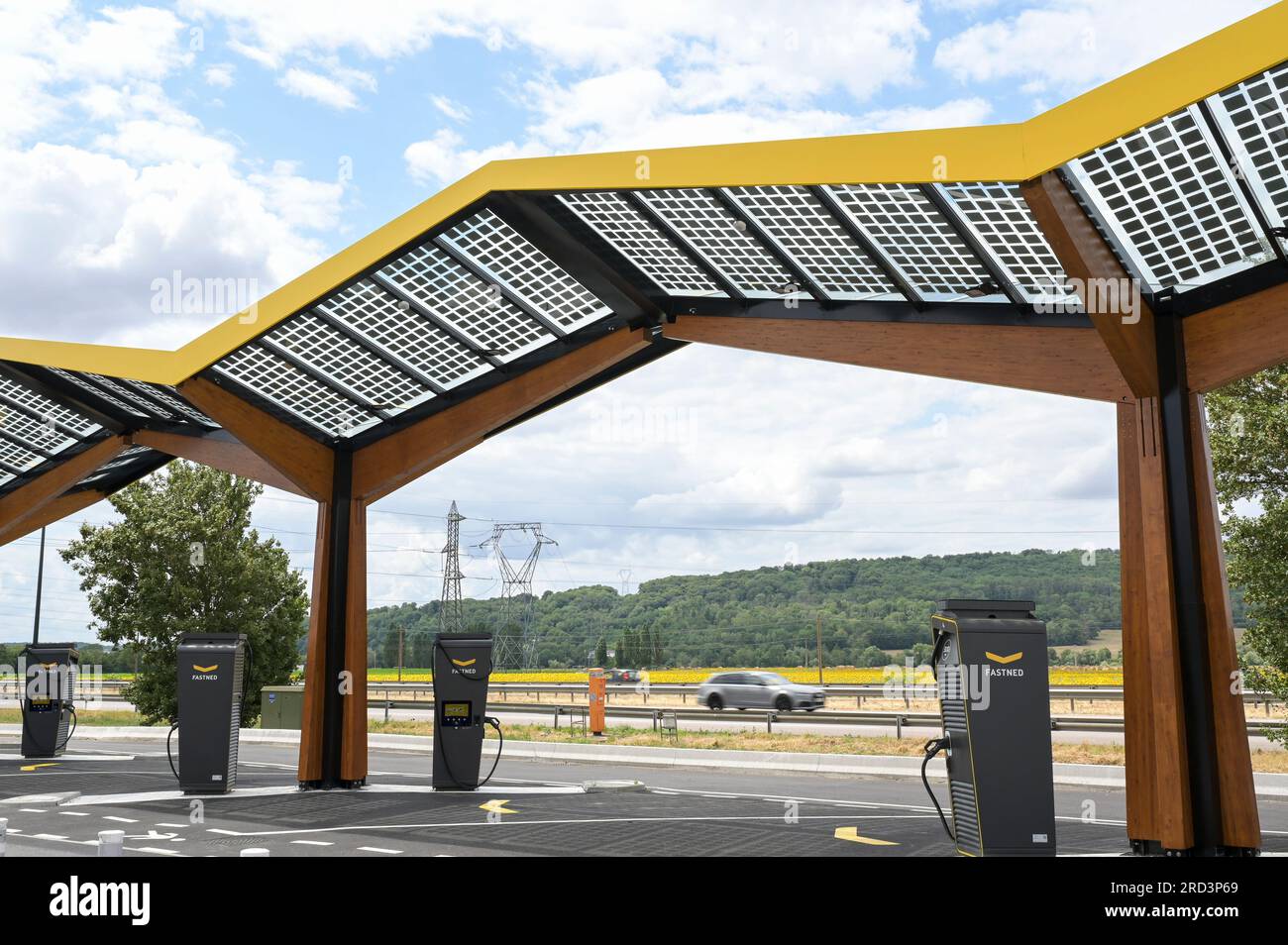 FRANKREICH, Fastned Schnellladestation für Elektrofahrzeuge an der Autobahn, Solarzellen auf Dach / FRANKREICH, Fastned Stromladestation für Elektrofahrzeuge an Dyneff Tankstelle an der Autobahn, Solarzellen auf Dach, Hintergrund Sonnenblume Feld Stockfoto