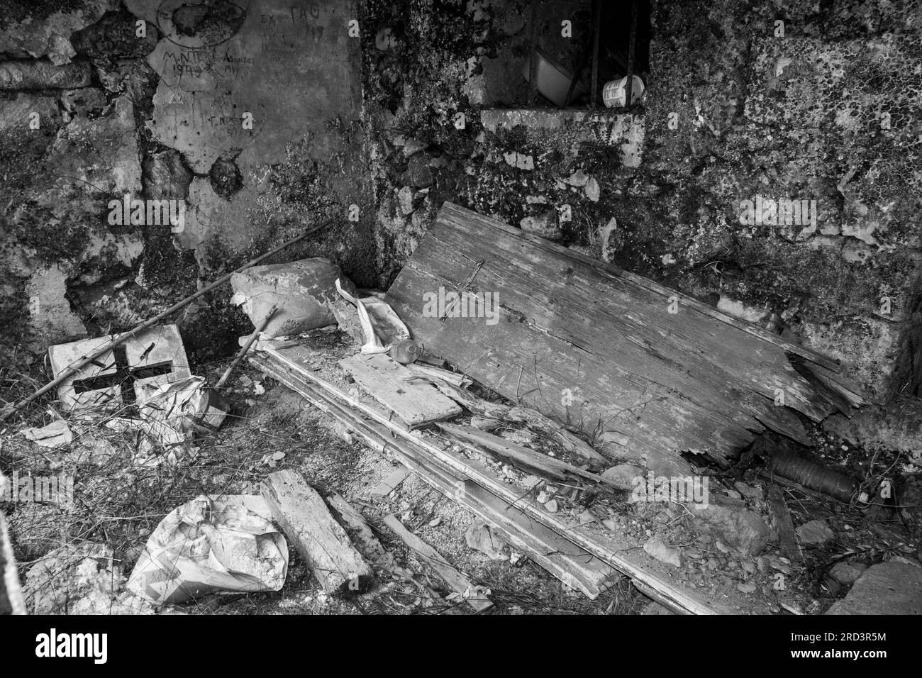 Ein zerstörtes Steingebäude voller Bauschutt und Müll, einschließlich Holztür mit festem Kreuz. Schwarzweißbild. Stockfoto