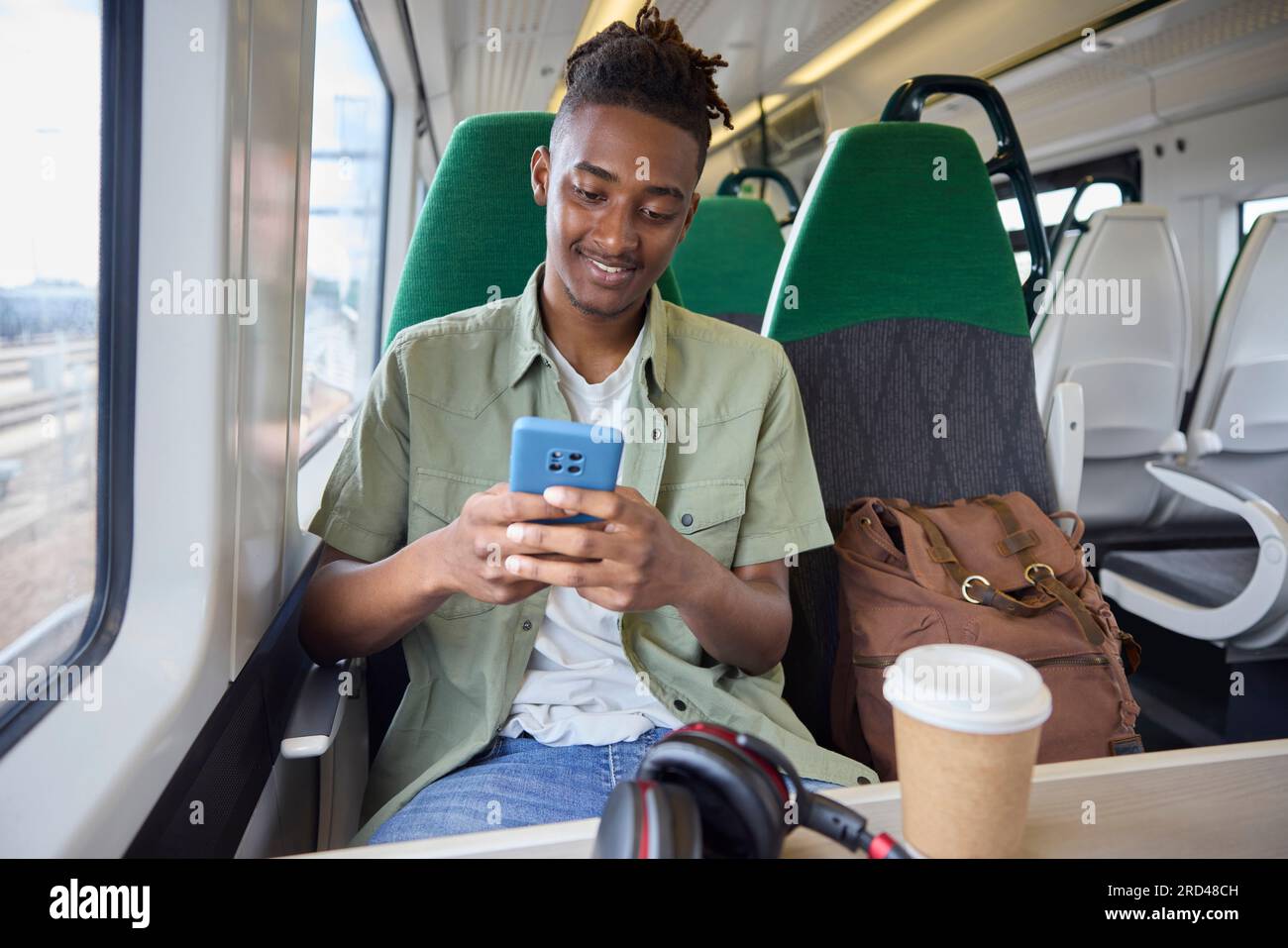 Junger Mann, Der Im Zug Zur Arbeit Pendelt, Sitzt Im Zug Und Schaut Auf Ein Mobiltelefon Für Reiseinformationen Oder Soziale Medien Stockfoto