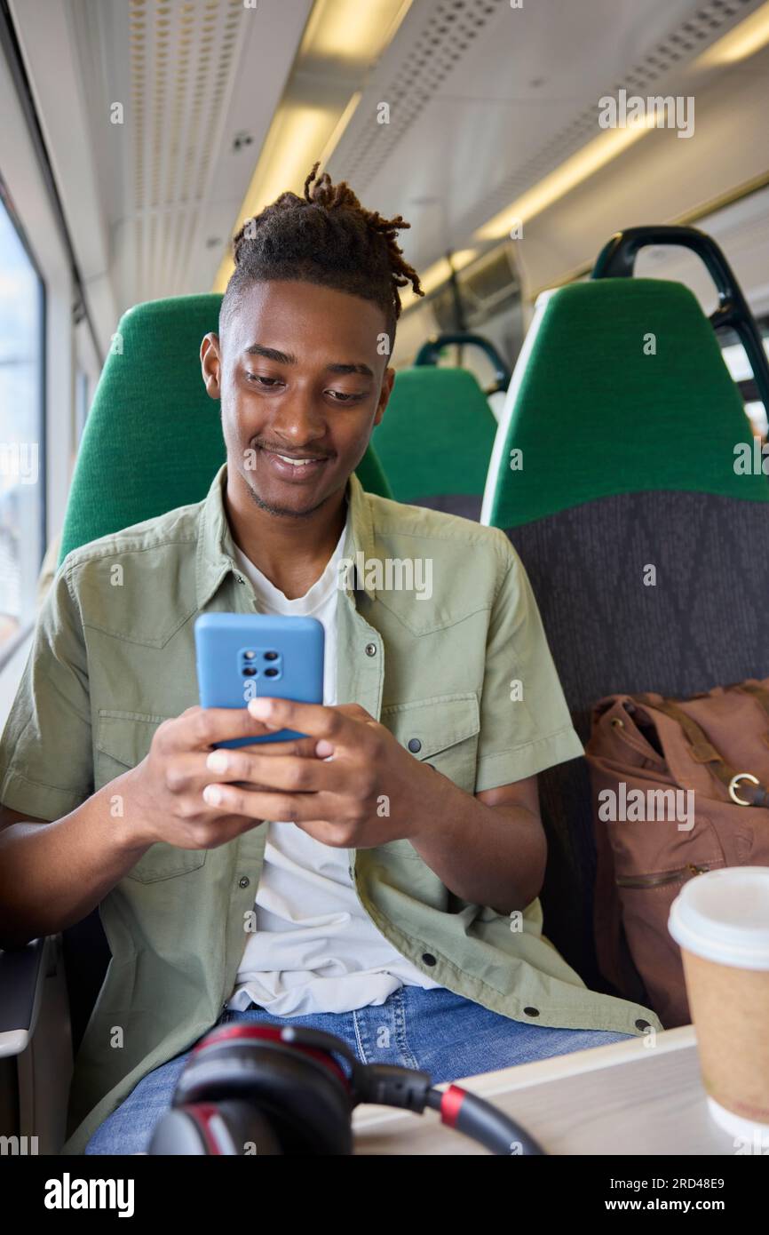 Junger Mann, Der Im Zug Zur Arbeit Pendelt, Sitzt Im Zug Und Schaut Auf Ein Mobiltelefon Für Reiseinformationen Oder Soziale Medien Stockfoto