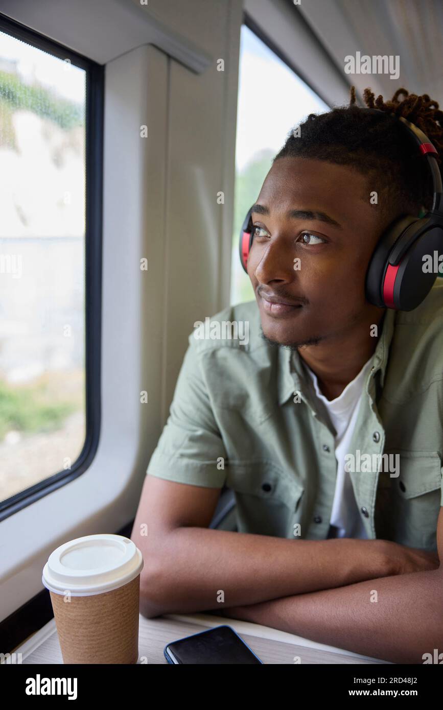 Junger Mann, Der Zur Arbeit Pendelt, Sitzt Im Zug Und Trägt Kabellose Kopfhörer Mit Blick Aus Dem Fenster Stockfoto