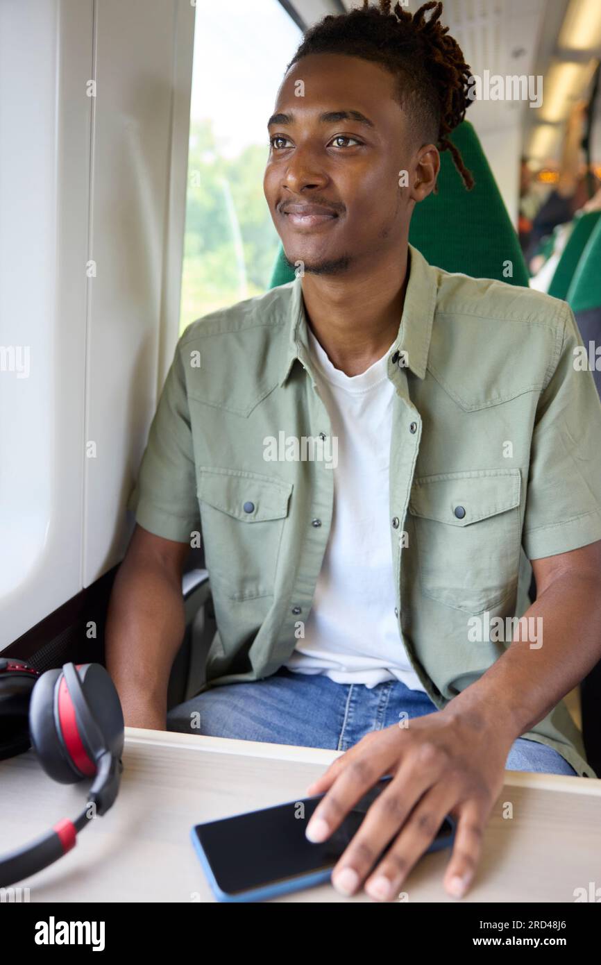 Junger Mann Auf Dem Weg Zur Arbeit, Sitzt Im Zug Mit Kabellosen Kopfhörern Und Mobiltelefon Stockfoto