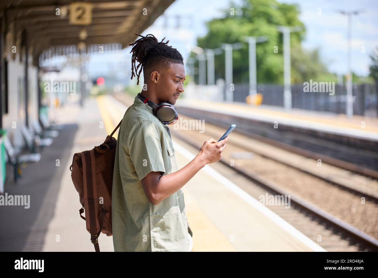 Junger Mann, Der Im Zug Zur Arbeit Pendelt, Steht Auf Der Plattform Und Schaut Auf Ein Mobiltelefon Für Reiseinformationen Oder Soziale Medien Stockfoto