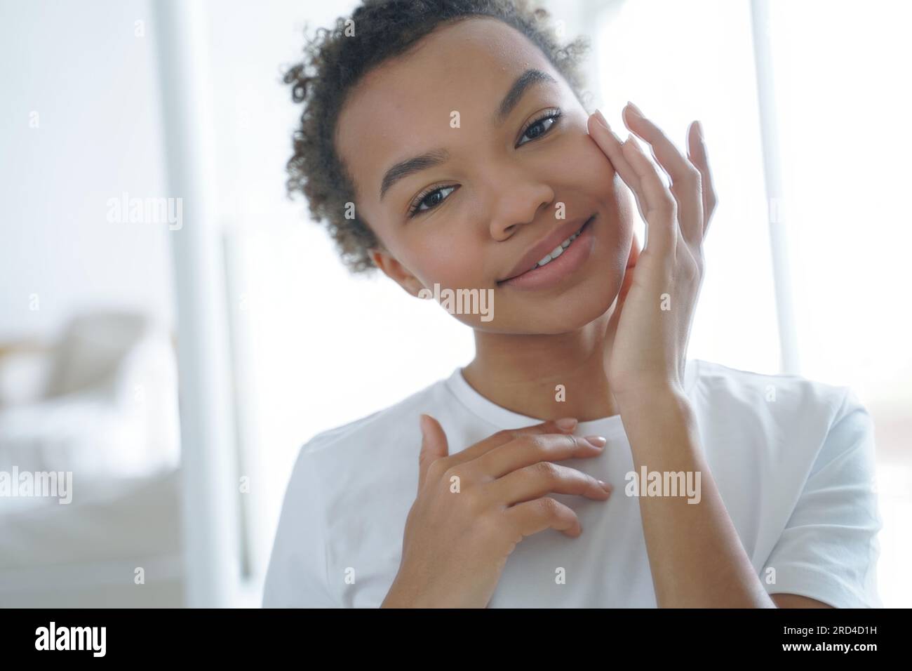 Ein hübsches afroamerikanisches Mädchen liebt Hautpflege, pflegt feuchtigkeitsspendende Creme, strahlt natürliche Schönheit aus. Stockfoto