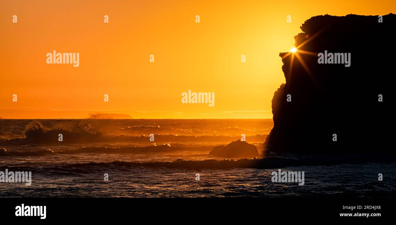 Klippen an der Küste, die vor dem pulsierenden Sonnenuntergang über den Wellen des Ozeans abgeschirmt sind. Stockfoto