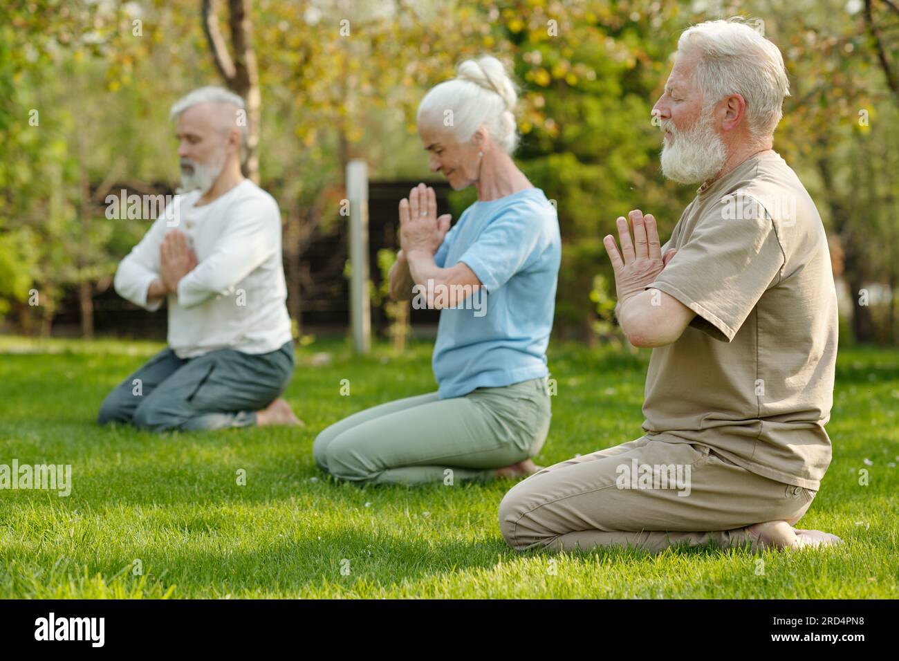 Konzentrieren Sie sich auf einen bärtigen Seniorenmann, der die Hände an der Brust zusammenhält, während er mit anderen Patienten des Altersheimes Yoga übt Stockfoto