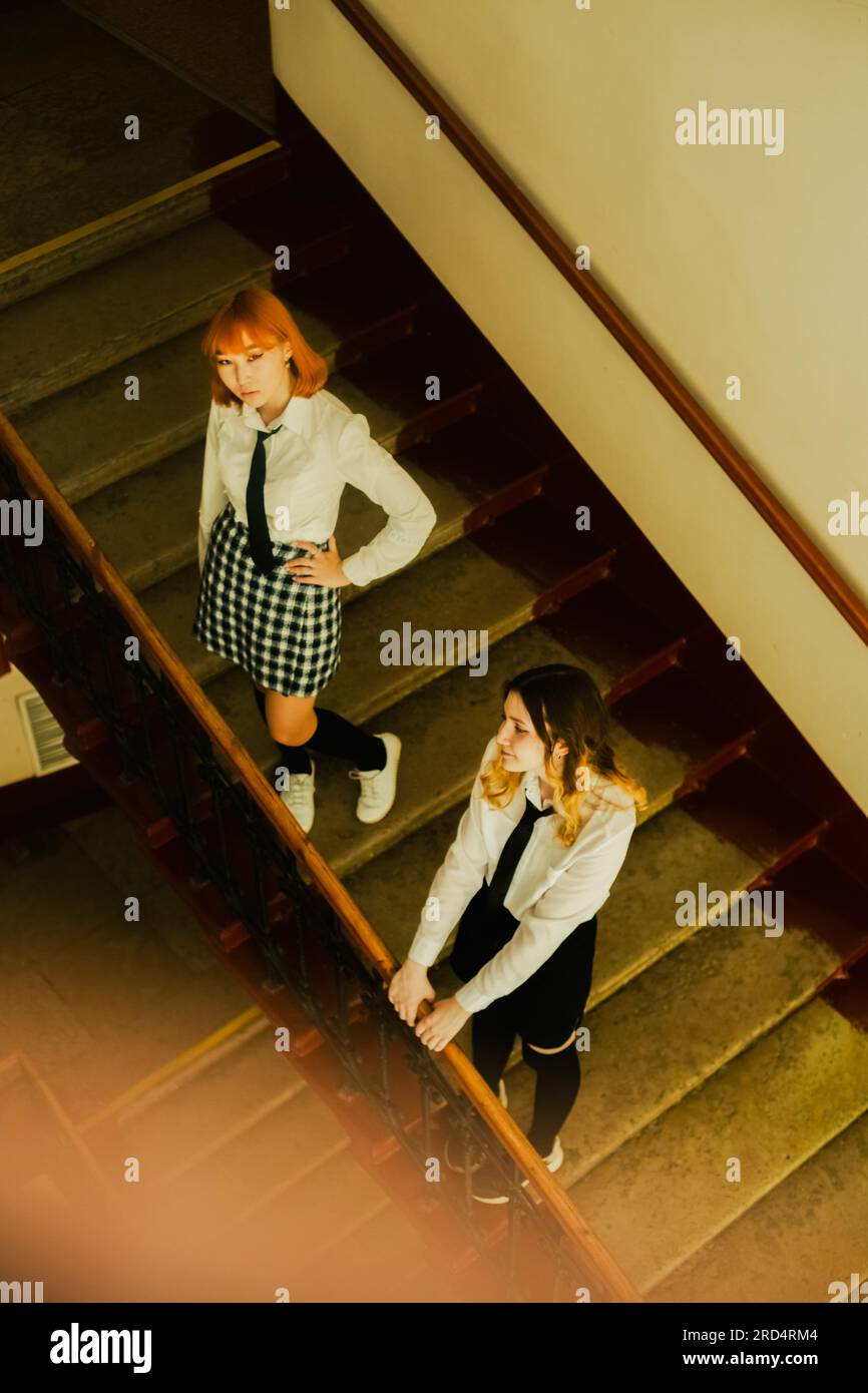 Zwei Schulmädchen, gekleidet in Schuluniformen, stehen an einem Schultag neben dem Treppengeländer. Sie sind Freunde. Stockfoto