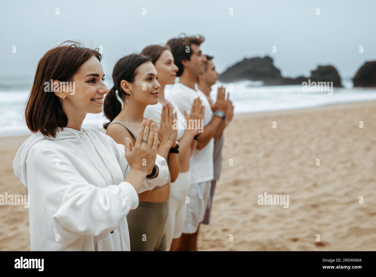 Gruppe junger Frauen und Männer, die während ihres Morgenübens am Strand am Meer meditieren, freier Raum Stockfoto