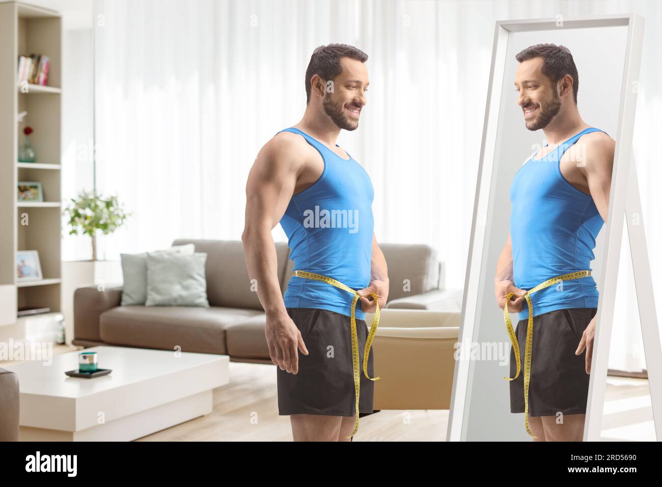 Passen Sie den Mann in Sportbekleidung mit Taillenumfang vor einem Spiegel zu Hause an Stockfoto