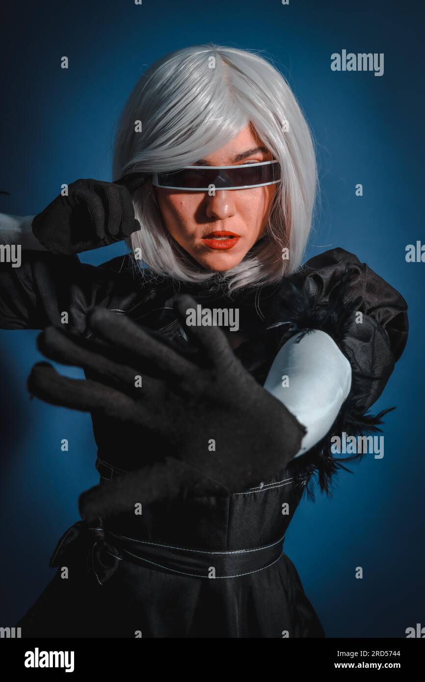 Porträt einer Cosplay-Frau in schwarzem Kostüm und einer weißen Perücke im Studio auf blauem Hintergrund Stockfoto