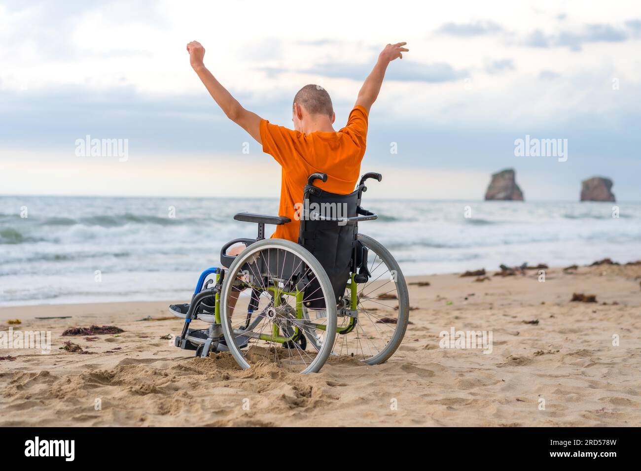 Ein behinderter Mensch auf dem Rücken im Rollstuhl am Strand mit offenen Armen, der die Freiheit des Meeres und der Natur genießt Stockfoto