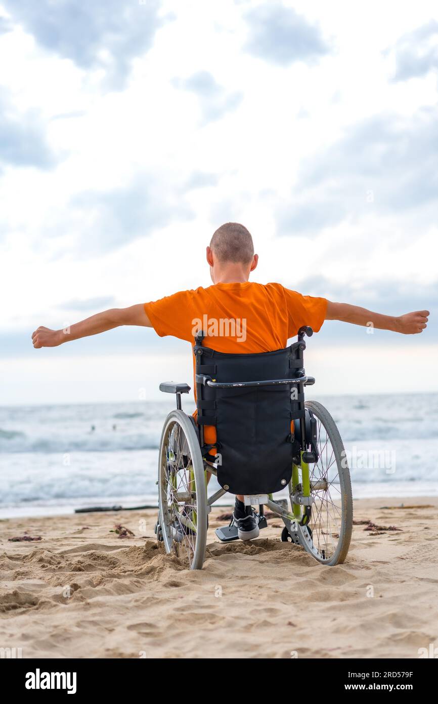 Ein behinderter Mensch auf dem Rücken im Rollstuhl am Strand, der sich frei fühlt Stockfoto