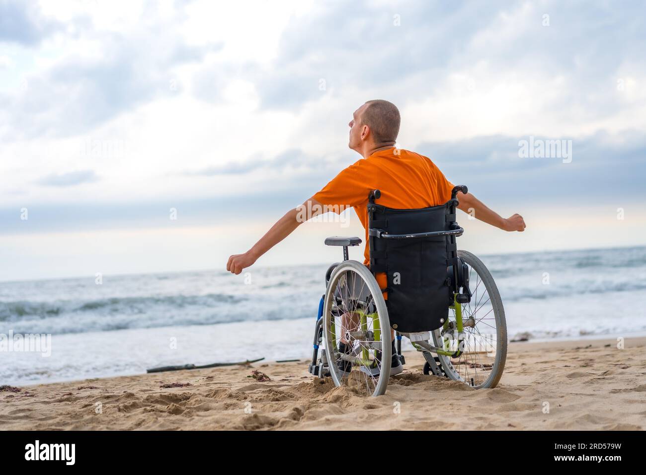 Ein behinderter Mensch auf dem Rücken im Rollstuhl am Strand fühlt sich frei am Meer Stockfoto