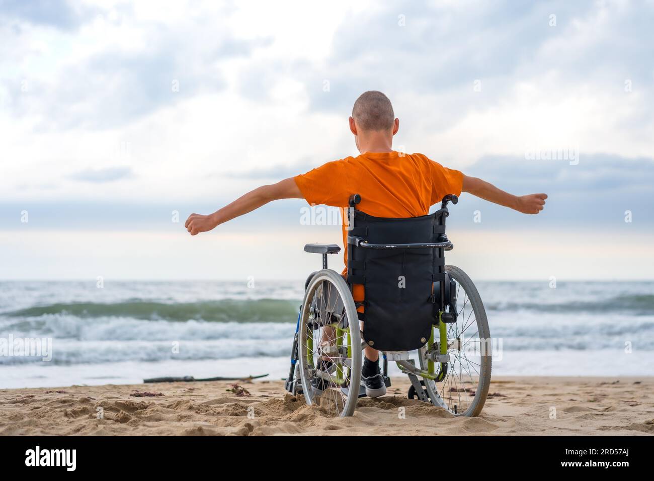 Ein behinderter Mensch auf dem Rücken im Rollstuhl am Strand, der sich frei fühlt Stockfoto