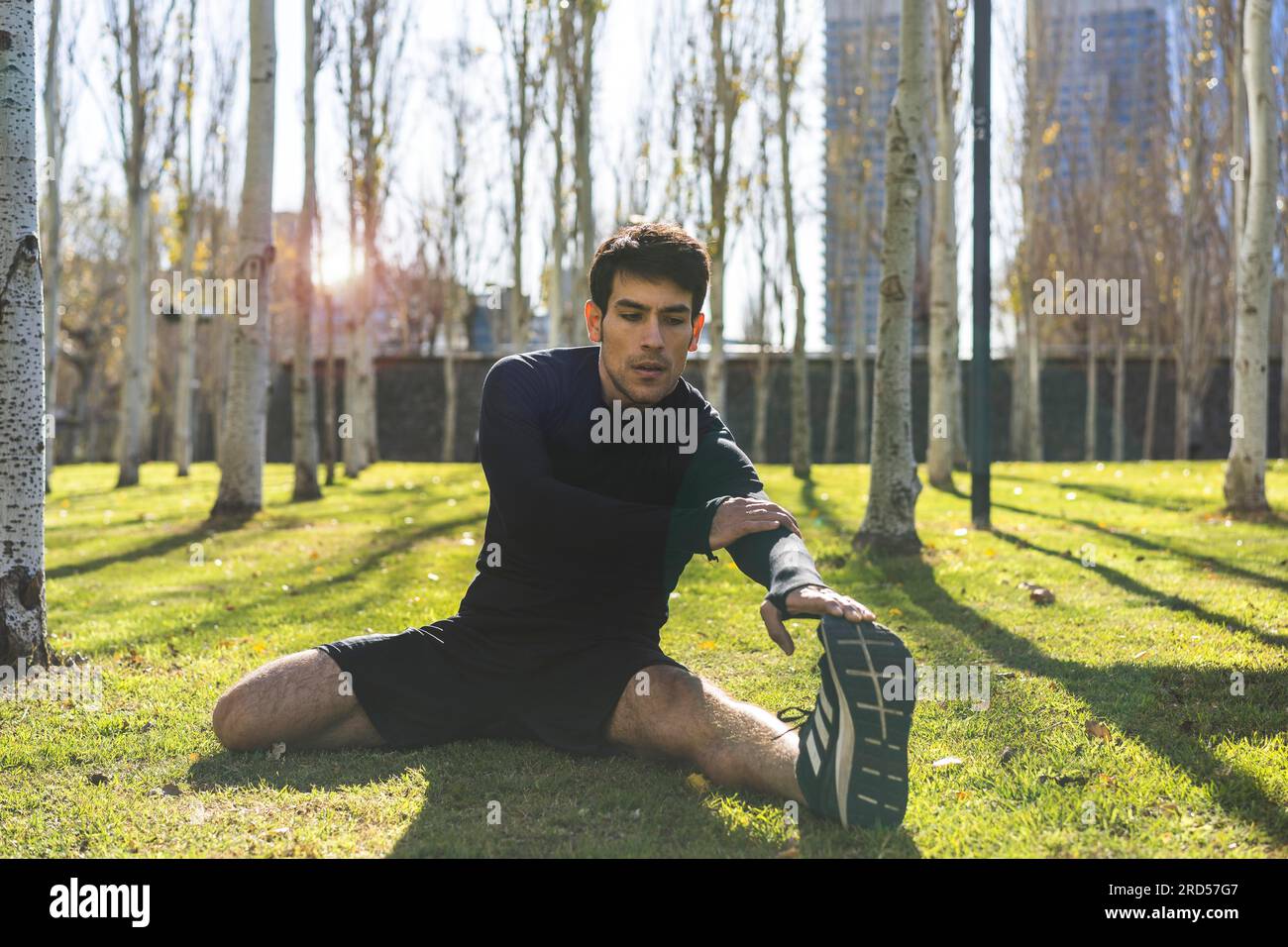 Sportlicher gutaussehender Mann, der sich nach dem Joggen im öffentlichen Stadtpark Beine vertreten konnte Stockfoto