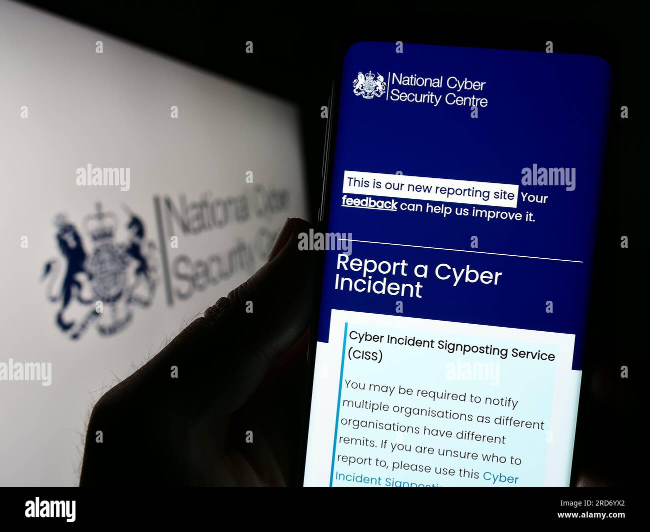 Person, die ein Mobiltelefon mit einer Website des National Cyber Security Centre (NCSC) des Vereinigten Königreichs auf dem Bildschirm vor dem Logo hält. Konzentrieren Sie sich auf die Mitte des Telefondisplays. Stockfoto