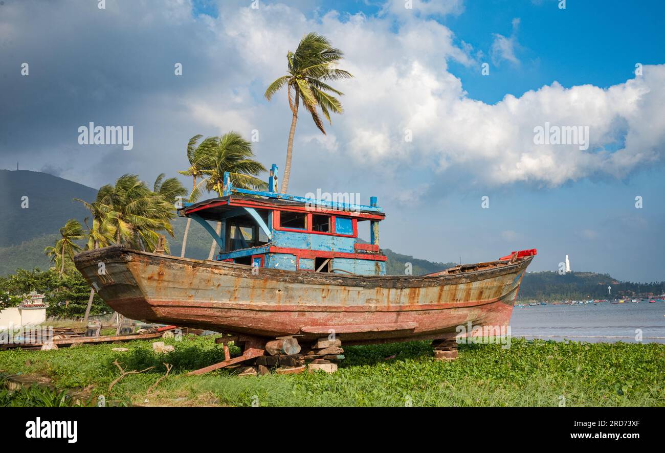 Ein zerschmettertes und unseetaugliches blaues und rotes Fischerboot aus Holz, das sich auf Häuserblocks neben dem Pham Van Dong Strand in Son Tra, Danang, Vietnam, befindet. Stockfoto