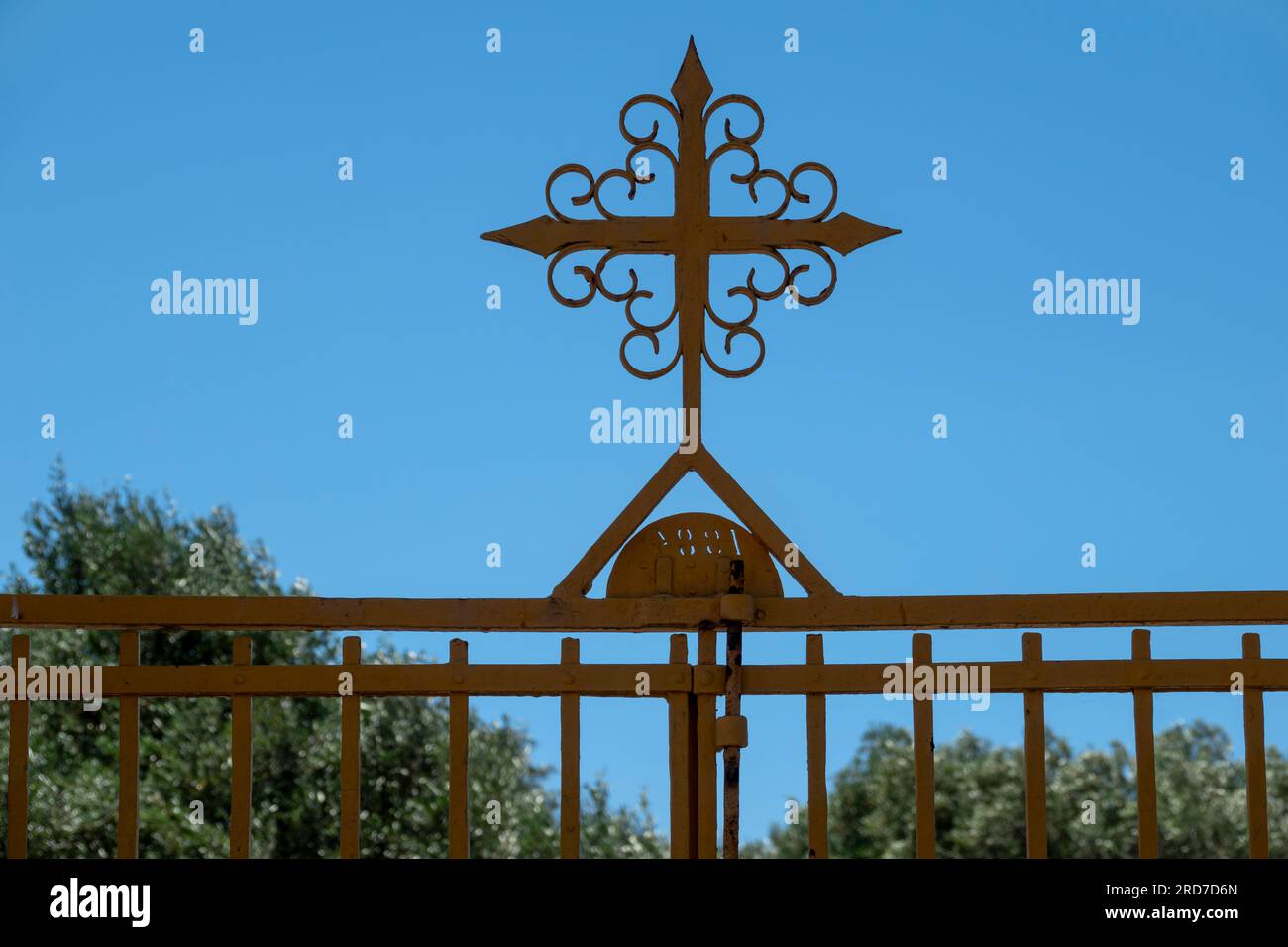 Schmiedeeisen und bemalter Stahl Kirchentor mit dekorativem Kreuz und Sträuchern im Hintergrund Stockfoto