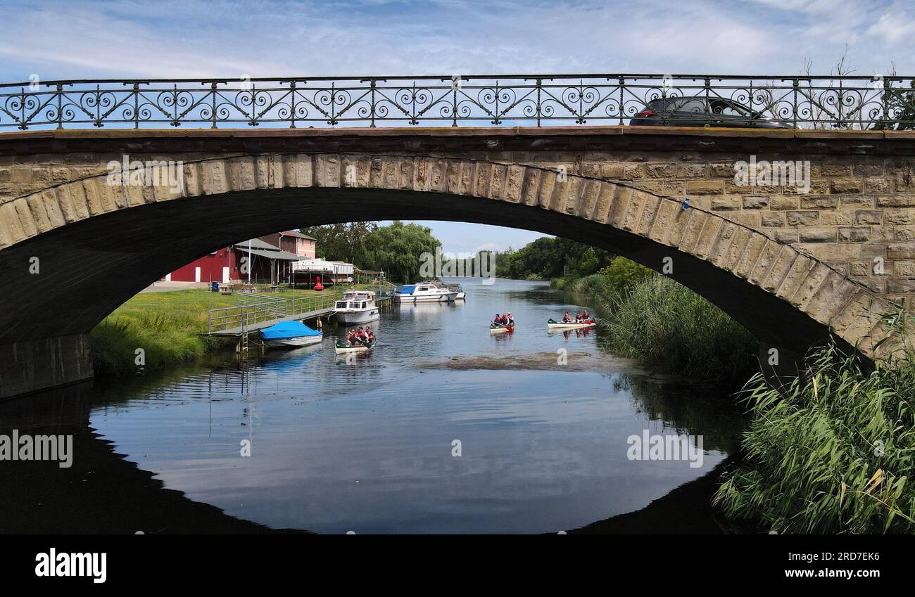 Nienburg, Deutschland. 19. Juli 2023. Wassersportbegeisterte sitzen in drei Kanus und fahren unter einer Brücke auf dem Bode in der Nähe von Nienburg (Saale). Um die Region für Wasserwanderer attraktiver zu machen, sollen neue Treppen gebaut werden, die ihnen helfen, auf das Wasser zu gelangen. Kredit: Simon Kremer/dpa/Alamy Live News Stockfoto